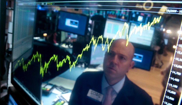 In this 2014 photo, specialist Jay Woods is reflected in a screen at his post that shows five years of the Dow Jones industrial average on the floor of the New York Stock Exchange.