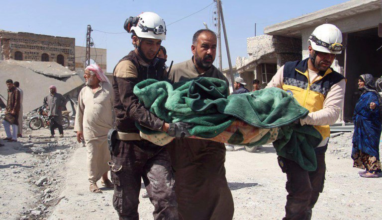 This photo provided by the Syrian Civil Defense group known as the White Helmets shows members of the Syrian Civil Defense workers carrying a victim after a deadly airstrike hit a market killing several people in the village of Ras el-Ain, in the northwestern province of Idlib, Syria.
