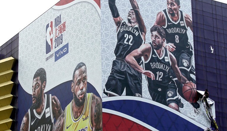 A worker takes down a billboard advertising an NBA preseason basketball game on Thursday between the Los Angeles Lakers and Brooklyn Nets in Shanghai, China, Wednesday, Oct. 9, 2019. The NBA has postponed Wednesday's scheduled media sessions in Shanghai for the Brooklyn Nets and Los Angeles Lakers, and it remains unclear if the teams will play in China this week as scheduled.