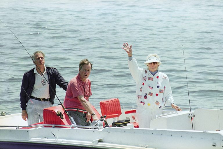 Pres. George H. W. Bush, center, and First Lady Barbara Bush, right, wave from their boat Fidelity as stopped at a local eatery, Sunday, July 2, 1989, Cape Porpoise, Maine. The Bushes are vacationing at their home on the Maine coast for the holiday weekend. The man on the left is unidentified.
