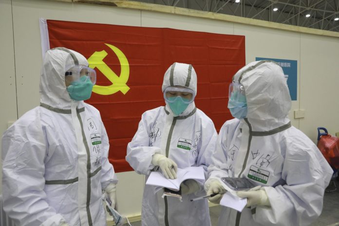 In this photo taken Feb. 8, 2020 and released by Xinhua News Agency, medical workers discuss patients' treatment near a Communist Party flag at the "Wuhan Living Room" temporary hospital in Wuhan, central China's Hubei Province. As the rest of the world grapples with a burgeoning virus outbreak, China's ruling Communist Party has turned to its propaganda playbook to portray its leader as firmly in charge, leading an army of health workers in a "people's war" against the disease.