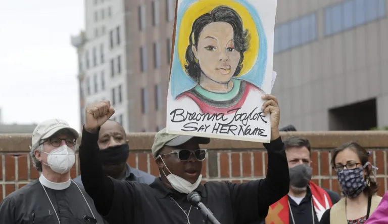 Kevin Peterson, the founder and executive director of the New Democracy Coalition, center, displays a placard showing Breonna Taylor as he addresses a rally.