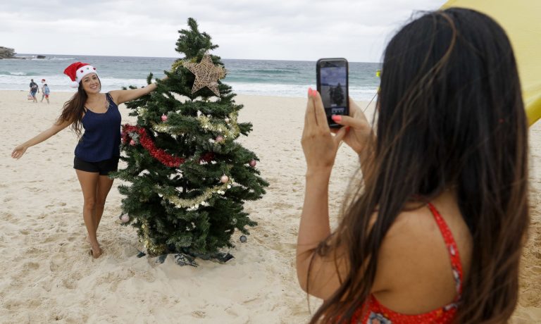 Milena Ussa of Colombia, right, takes a photo of her friend Fernanda Gonzalez of Mexico with a Xmas tree on Christmas Day at Sydney's Bondi Beach, Australia, Friday, Dec. 25, 2020. 