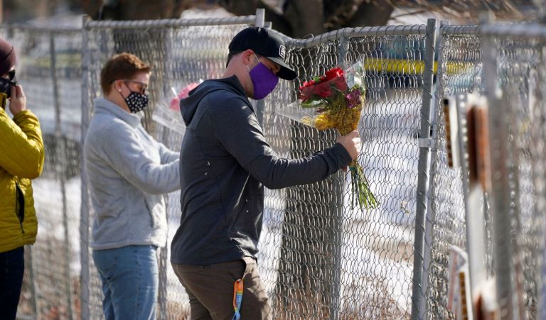 Kiefer Johnson places a bouquet of flowers into a makeshift fence put up around the parking lot outside a King Soopers grocery store where a mass shooting took place a day earlier, in Boulder.