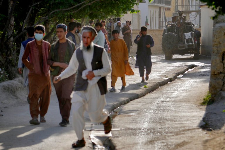 People leave the site of an explosion as a Taliban fighter stands guard in Kabul, Afghanistan, Friday, April 29, 2022. A powerful explosion ripped through a mosque in the Afghan capital of Kabul on Friday, killing at least 10 people and wounding 20, a Taliban spokesman said. 
