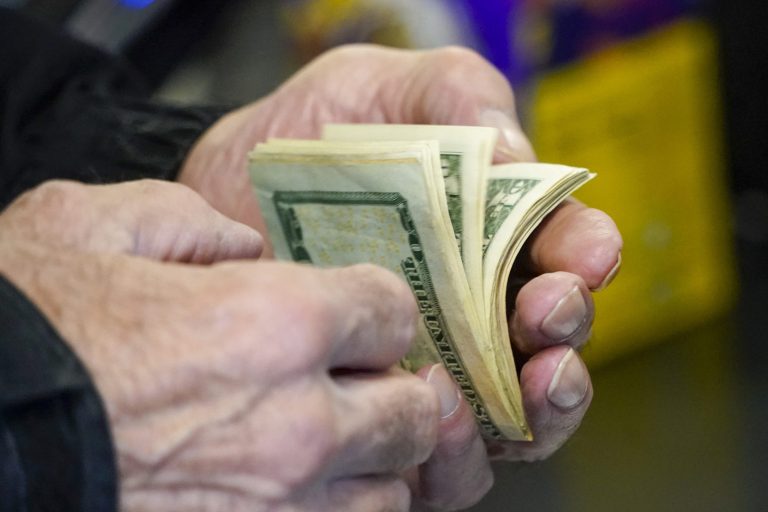 A customer thumbs through his money as he buys tickets for the Monday Powerball drawing with an annuity value of at least $1.9 billion, Monday, Nov. 7, 2022, at a convenience store in Renfrew, Pennsylvania. (AP Photo/Keith Srakocic)