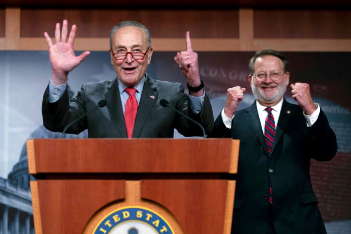 Senate Majority Leader Chuck Schumer (D-NY) joined by Sen. Gary Peters (D-MI), chairman of the Democratic Senatorial Campaign Committee, signals "51" as he speaks with reporters in Washington on Dec. 7, 2022.