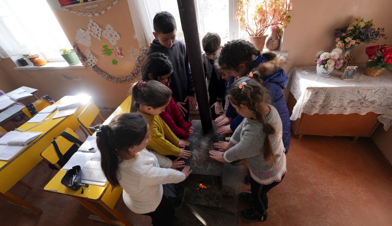 Nagorno-Karabakh schoolchildren warm themselves around a stove in the classroom in Stepanakert, the capital of the separatist region of Nagorno-Karabakh, also known as Artsakh, on Thursday, Dec. 15, 2022. Protesters claiming to be ecological activists have blocked the only road leading from Armenia to Nagorno-Karabakh for more than a month, leading to increasing food shortages. Local authorities have called for a humanitarian airlift for critical supplies, but Azerbaijan has not authorized the region's airport to operate.