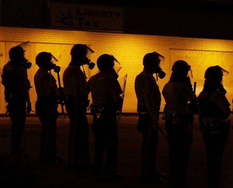 Police wait to advance after tear gas was used to disperse a crowd Sunday during a protest for Michael Brown, who was killed by a police officer last Saturday in Ferguson, Mo. (AP Photo/Charlie Riedel)