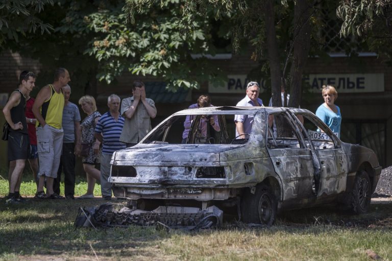 Local people look at a burnt-out car following a shelling from Ukrainian government forces, in Slovyansk, Ukraine, Wednesday, May 28, 2014.  In Slovyansk, a city 90 kilometers (55 miles) north of Donetsk which has seen many clashes over the past few weeks, residential areas came under mortar shelling Wednesday from government forces. The school was badly damaged along with other buildings, and residents told The Associated Press that several people were wounded. (AP Photo/Alexander Zemlianichenko)