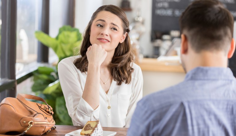 Young woman makes an uneasy or disinterested face while on a blind date in a coffee shop. The back of the young man's head is seen in the foreground.