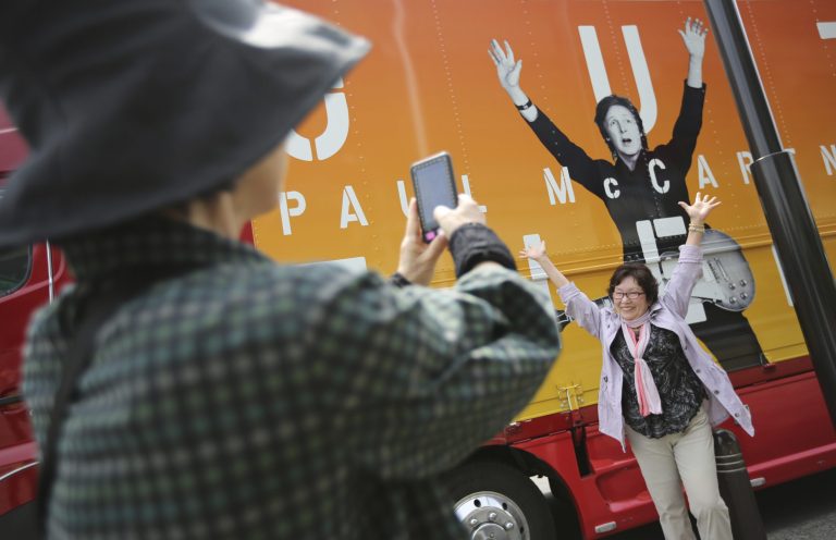 Fans take photos in front of a promotional truck bearing an image of Paul McCartney at Nippon Budokan hall in Tokyo, Tuesday, May 20, 2014. Paul McCartney is canceling his entire Japan tour because of illness including the one set for Wednesday at Nippon Budokan hall, where The Beatles performed during their first Japan tour in 1966. (AP Photo/Eugene Hoshiko)