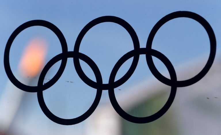 The flame of the Olympic cauldron is viewed through a glass panel with a sticker of the Olympic rings at a food court in Olympic Park in Sochi, Russia, during the 2014 Winter Olympics, Wednesday, Feb. 12, 2014. (AP Photo/Julio Cortez)