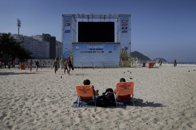 Two men relax in front of a giant screen for soccer fans to watch live broadcast of the World Cup soccer matches on the Copacabana beach in Rio de Janeiro, Brazil, Monday, June 16, 2014. Rio de Janeiro is one of the host cities for the 2014 World Cup soccer tournament.(AP Photo/Wong Maye-E)