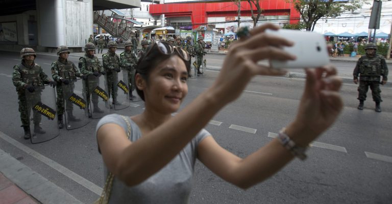 A woman stops to take a selfie with Thai soldiers stand guard near Victory Monument in Bangkok, Thailand, Friday, May 30, 2014. An anti-coup activist called Friday for a weekend rally to defy the military government's ban on demonstrations, urging those opposed to the takeover to wear masks and be ready for cat-and-mouse chases with soldiers in the capital. (AP Photo/Sakchai Lalit)