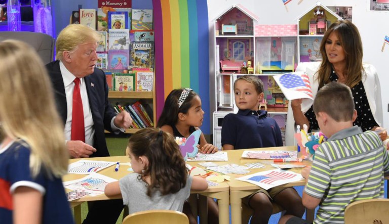 President Trump (left), and his wife Melania (fourth to the right), are pictured coloring images with kids at a hospital.