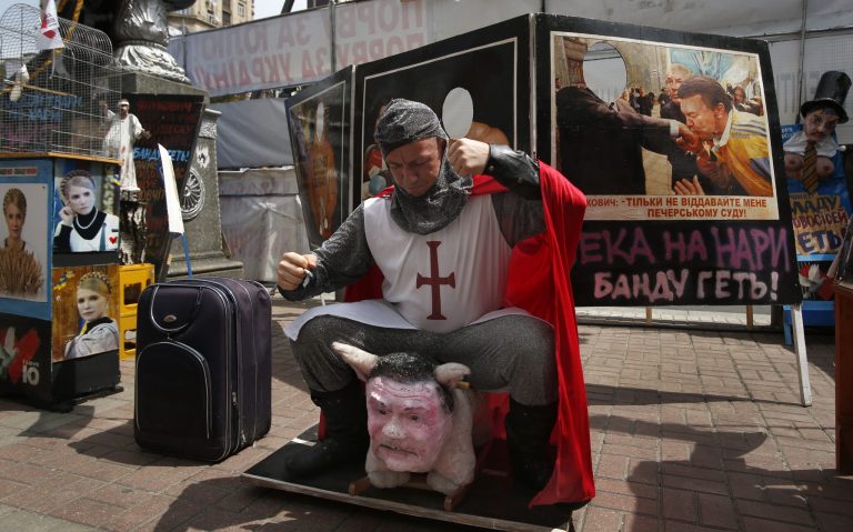   In this Thursday, June 14, 2012 photo Stan Stanfield, the captain of an unofficial England football fan team pretends to ride a pig with a head depicting Ukrainian President Viktor Yanukovych in a protest camp set up by opposition groups in Kiev, Ukraine. Supporters of jailed former Ukrainian Prime Minister Yulia Tymoshenko hope to use Euro 2012 to press for her release. (AP Photo/Sergei Grits)  