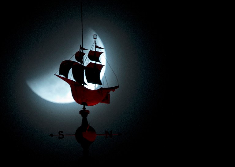 The Earth's shadow begins to fall on the moon during a total lunar eclipse, behind a weathervane shaped like a Spanish galleon on the Freedom Tower, Wednesday, Oct. 8, 2014 in Miami. (AP Photo/Wilfredo Lee)