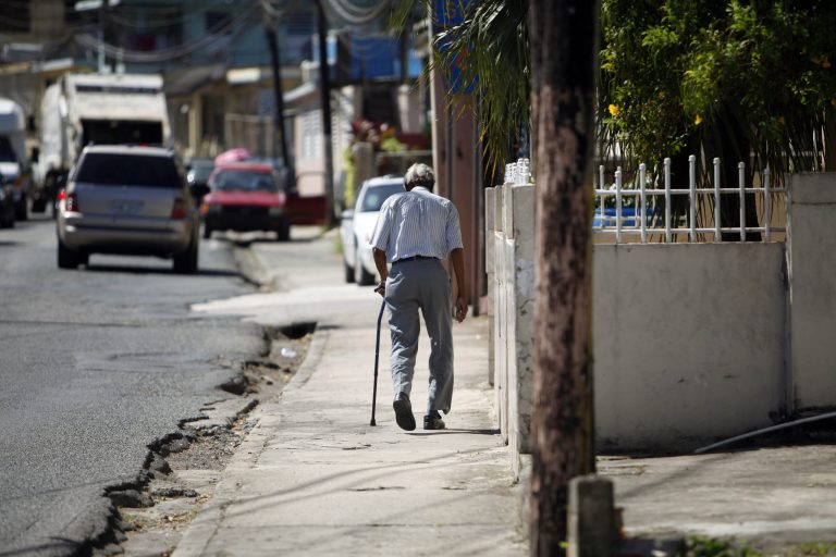 In this Nov. 14, 2013 photo, Mariano Perez Morales, 75, walks a sidewalk in Barceloneta, Puerto Rico. Retirees are struggling with rising water, power and other utility prices, which the government hiked to trim a budget deficit projected to hit $820 million this year. The weak economy also has reduced pensions for retired Puerto Rican public workers. (AP Photo/Ricardo Arduengo)