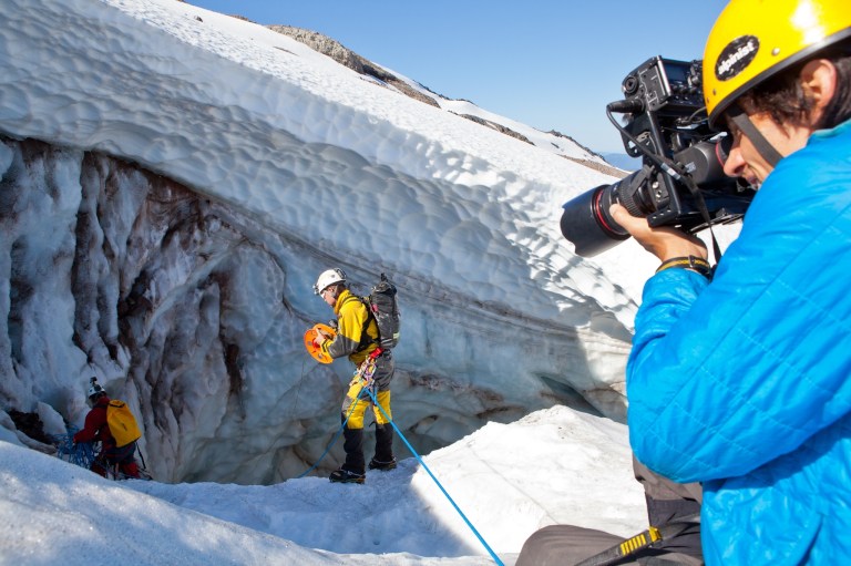 In this 2013 photo provided by Oregon Field Guide, photographer Andy Maser, right, photographs caver Eddy Cartaya, center, near a glacier cave in the Mount Hood Wilderness area in Oregon for an episode of 