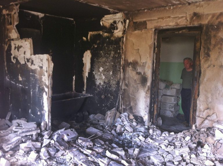 In this image taken Saturday Aug. 16, 2014 a man shows his neighbour's apartment that was burned down after a  missile hit a residential area in Lysychansk, Ukraine, during the fighting between the Ukrainian army and the pro-Russian rebels. Lysychansk was retaken by Ukrainian army late last month but has seen sporadic clashes until earlier last week.  After months of rebel occupation and weeks of Ukrainian liberation, the residents of Lysychansk this shell-shocked border town say they hope simply to rebuild their former lives _ but fear the return of war to their doorstep. (AP Photo/Vitnija Saldava)