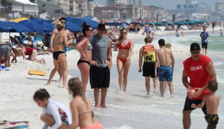 Beachgoers enjoy a sunny day in Destin, Florida on Wednesday, March 18, 2020.  The threat posed by coronavirus didn't seem to deter vacationers to this Florida panhandle community from spending the day on a crowded beach. The Okaloosa County (Florida) Sheriffâs Office announced that deputies would be patrolling the countyâs beaches to remind beachgoers to abide by Gov. Ron DeSantisâs emergency orders on social distancing and group sizes.