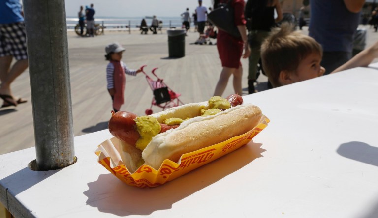 Pedestrians pass a Nathan's Famous hot dog Tuesday, May 20, 2014, in the Brooklyn borough of New York. 