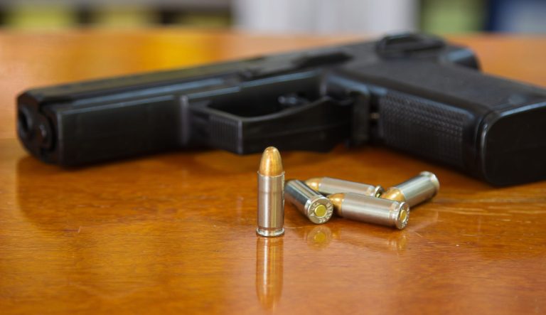 Handgun with ammunition on wood surface at home.