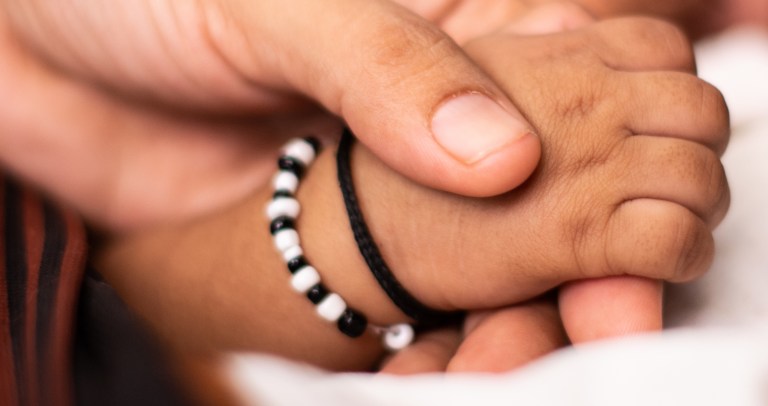 A newborn holds a parent's hand while sleeping in a cradle.