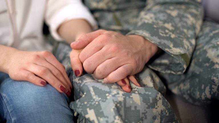 A male soldier holds his partner's hand.