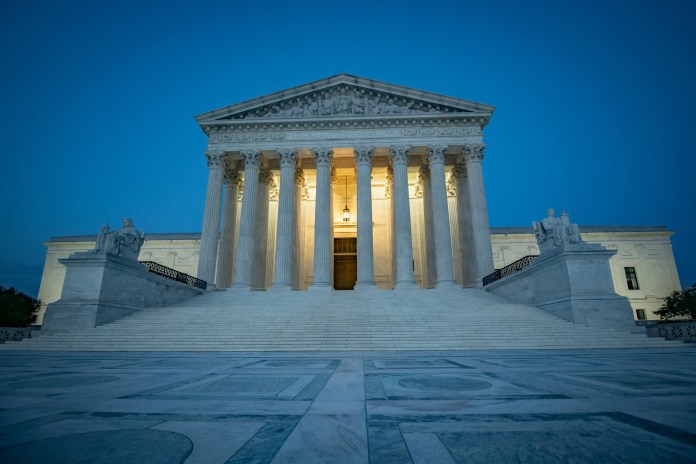 The sun flares in the camera lens as it rises behind the U.S. Supreme Court building.