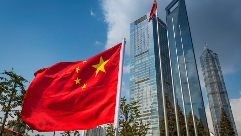 The vibrant red field and yellow stars of the Flag of the People's Republic of China flying in the breeze beside the futuristic glass and steel towers of Pudong's soaring skyscrapers, Shanghai, China. ProPhoto RGB profile for maximum color fidelity and gamut.