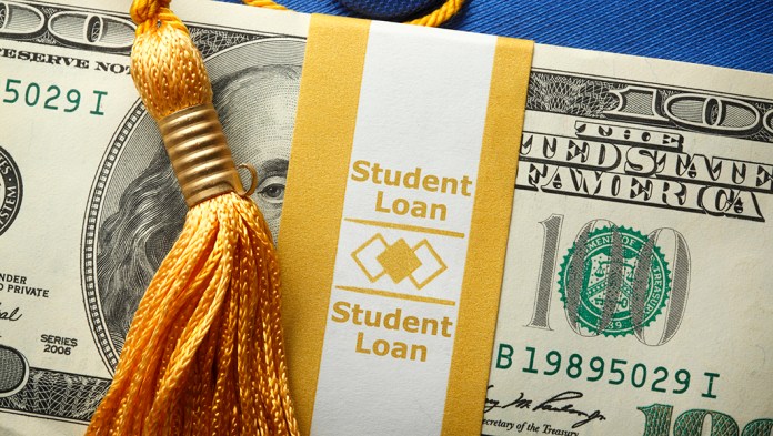 A stack of one hundred dollar bills in a money wrapper labeled "Student Loan" on top of a blue graduation cap. A gold graduation tassel is draped over the stack of money.
