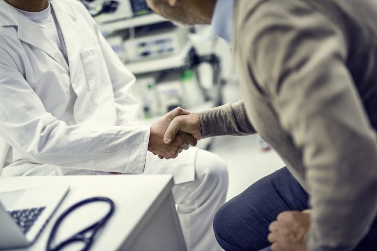 Doctor in white robes shakes hands with a patient in his office.