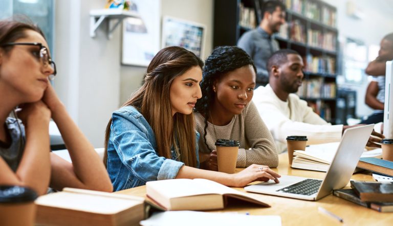 Shot of two young women using a laptop together in a college library.