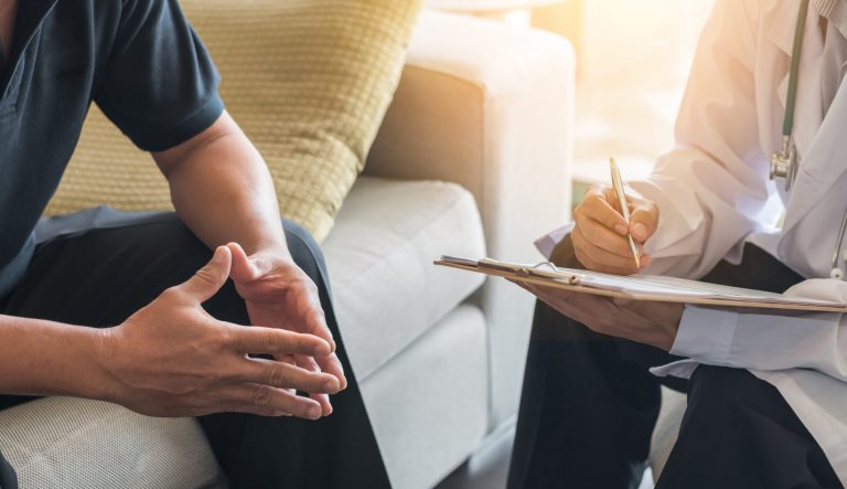 Doctor consulting male patient, working on diagnostic examination on men's health disease or mental illness, while writing on prescription record information document in clinic or hospital office.