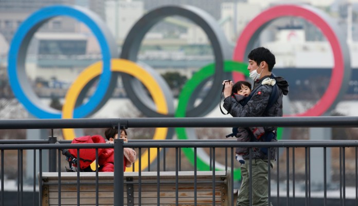 People wearing face masks to protect against the spread of the coronavirus stand at the Odaiba waterfront as Olympic rings is seen at the background in Tokyo, Tuesday, Jan. 26, 2021.