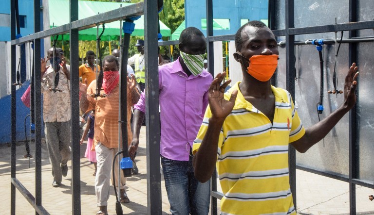 Ferry commuters walk through an automated disinfecting machine installed this week that sprays disinfectant onto all passengers boarding or disembarking ferries that cross the harbor of Mombasa, on the south coast of Kenya Wednesday, April 8, 2020. Kenya this week increased its restrictions to combat the coronavirus, announcing travel bans into and out of the capital city, Nairobi, the port of Mombasa and two counties.