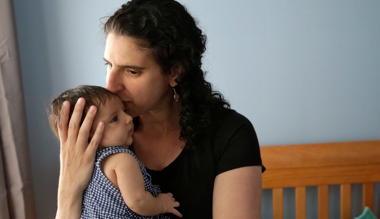 In this Thursday, June 1, 2017 photo, Elena Tenenbaum kisses her eight-week-old baby Zoe while standing for a photograph at their home in Providence, R.I. Tenenbaum, a clinical psychology researcher, had her second daughter in April of 2017, and has been able to use Rhode Island's paid family leave program, which started in 2014 and covers four weeks of partial pay.