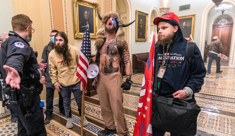 FILE - In this Wednesday, Jan. 6, 2021 file photo, supporters of President Donald Trump, including Jacob Chansley, center with fur and horned hat, are confronted by Capitol Police officers outside the Senate Chamber inside the Capitol in Washington. A video showed Chansley leading others in a prayer inside the Senate chamber. 