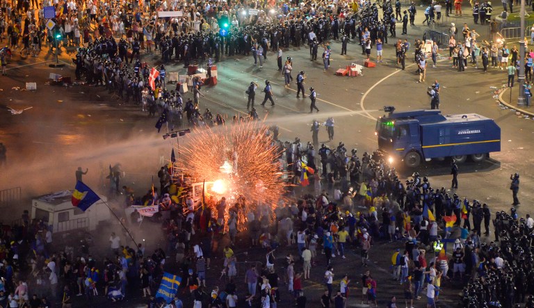 In this Friday, Aug. 10, 2018, photo, a teargas canister explodes as riot police charge using canon to clear the square during protests outside the government headquarters in Bucharest, Romania. Romanian authorities say hundreds of people including two dozen riot police have received medical treatment after an anti-government protest turned violent and two weapons were stolen from riot police officers.