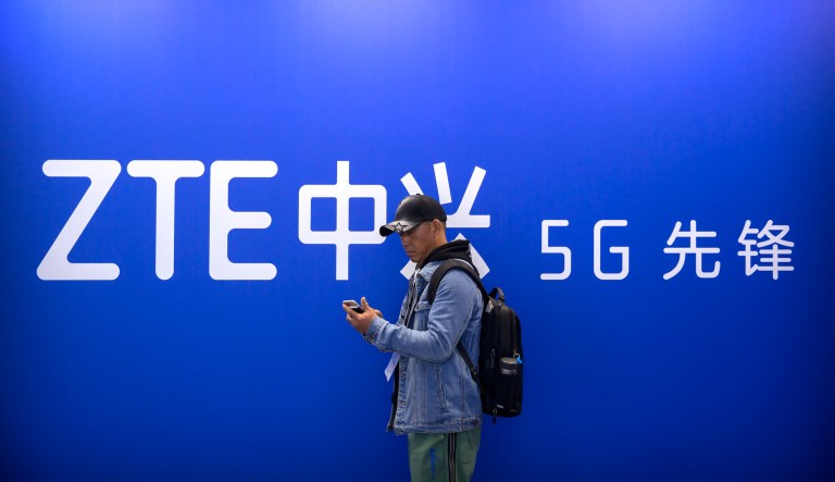 A man uses his smartphone near a display for 5G services from Chinese technology firm ZTE at the PT Expo in Beijing, Thursday, Oct. 31, 2019.