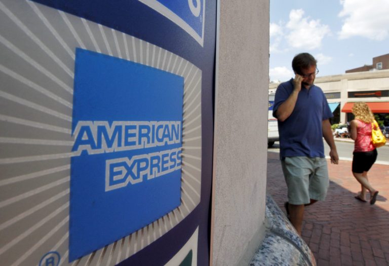 FILE - In this July 19, 2011 file photo, passers-by walk past an American Express logo near the entrance to a bank in the Harvard Square neighborhood of Cambridge, Mass. American Express Co.. reports quarterly financial results on Tuesday, July 29, 2014. (AP Photo/Steven Senne, File)
