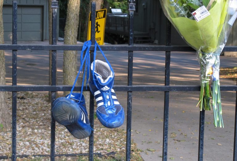   Wrestling shoes and flowers hang from the fence of the home of Ron and Rebecca Bramlage and their four children, left by friends and neighbors, Thursday, June 7, 2012, in Junction City, Kan. The family died in a Florida plane crash, and three Bramlage boys were wrestlers. (AP Photo/John Hanna)  