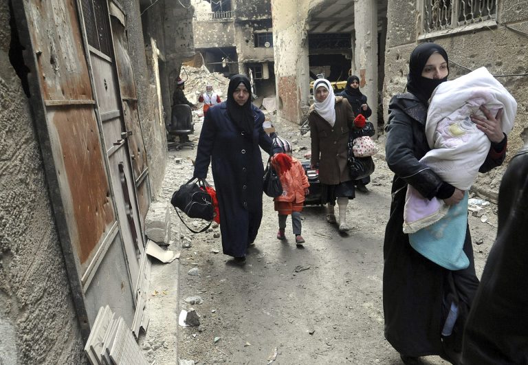 In this photo released by the Syrian official news agency SANA, residents of the besieged Yarmouk Palestinian refugee camp carry their belongings as they flee the camp, on the southern edge of the Syrian capital Damascus, Syria, Tuesday, Feb. 4, 2014. Over the past six days the U.N. continued to distribute food parcels in the Palestinian camp where activists say at least 85 people have died as a result of lack of food and medicine since mid-2013. (AP Photo/SANA)