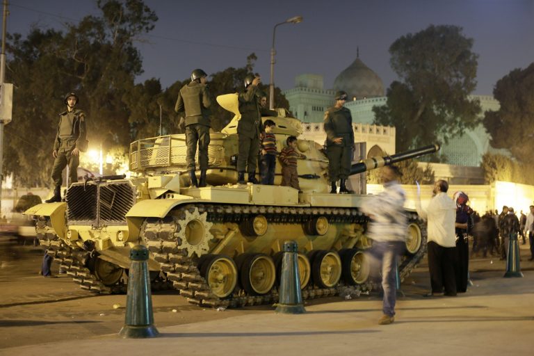   An Egyptian protester takes a picture with his mobile of his children on top of an Egyptian army tank outside the presidential palace, background, in Cairo, Egypt, Saturday, Dec. 8, 2012. Egypt's military warned Saturday of 'disastrous consequences' if the crisis that sent tens of thousands of protesters back into the streets is not resolved, signaling the army's return to an increasingly polarized and violent political scene.(AP Photo/Hassan Ammar)  