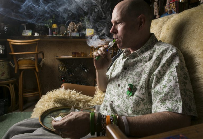 In this April 30, 2014 photo, Bill Britt, 54, who suffers from epileptic seizures and leg pain from a childhood case of polio, vaporizes medical marijuana at his home in Long Beach, Calif. Britt lives mostly on Social Security income and gets his supply for free from a friend whom he helps water and grow the plants. Insurers are reluctant to cover medical marijuana because of conflicting laws and lack of approval from the U.S. Food and Drug Administration. (AP Photo/Damian Dovarganes)