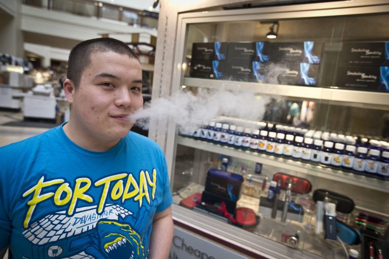 In this March 18, 2014 photo, Jesse Ly smoked his e-cigarette at the Smokeless Smoking kiosk at the Roseville Mall in Roseville, Minn. Supporters of defining electronic cigarettes in the same light as traditional tobacco products won a key round Monday, May 5 in the Minnesota Legislature. (AP Photo/The Star Tribune, Renee Jones Schneider)