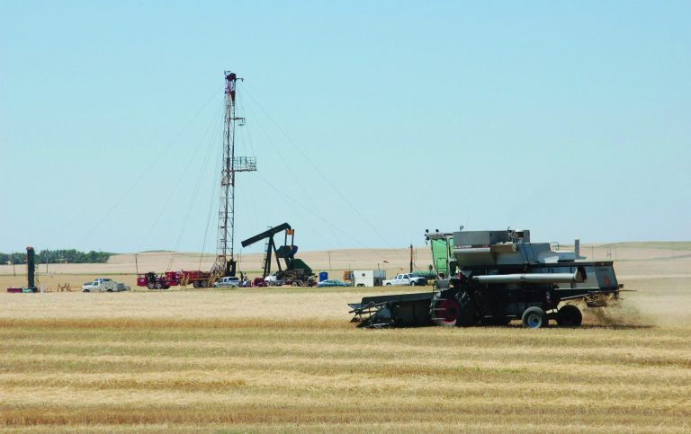 FILE - In this Aug. 19, 2008 file photo, a combine cuts durum near an oil well on Aug. 19, 2008, in Tioga, N.D. The worries about what drilling does to the air are both global and local, with scientists concerned about the effects on climate change as well as the possible health consequences from breathing smog, soot and other pollutants. (AP Photo/James MacPherson, file)