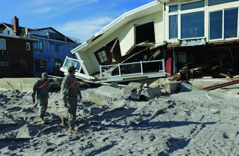 National Guardsmen Specialist Ivan Pimentel, left, and PFC Harry Cadet walk along the beach past a destroyed house during a break in their work in the Rockaways, Thursday, Jan. 10, 2013, in New York. The guardsmen said they were working with the New York City Office of Emergency Management going door-to-door to determine if residents needed portable heaters or other items to in the wake of Superstorm Sandy. Using portable personal tablets, they said they could provide residents with a heater within 30 minutes. (AP Photo/Kathy Willens)